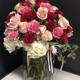 Bouquet of pink and red roses in a glass vase with a striped ribbon