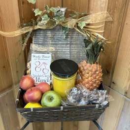 Fruit gift basket with pineapple, apples, peaches, candy, and a jar candle
