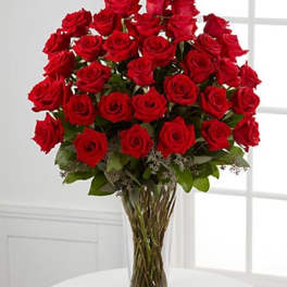 Tall arrangement of many red roses in a clear glass vase