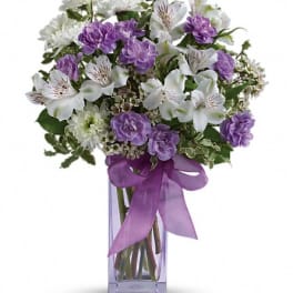 Purple and white bouquet in a clear glass vase with a purple ribbon