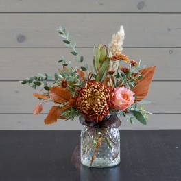 Orange and pink floral arrangement in a glass vase with a ribbon
