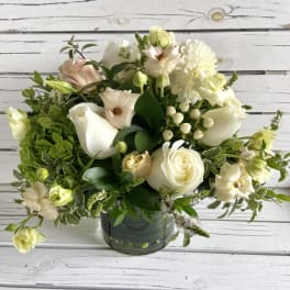 Round arrangement of white and cream flowers with soft green accents in a clear glass vase.