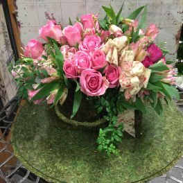 Pink roses and lilies arranged in a low moss-covered display