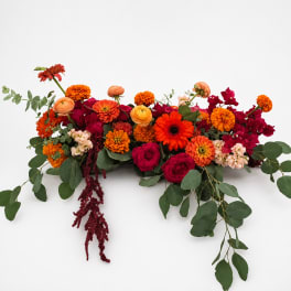 Long low arrangement of orange, red, and pink flowers with trailing greenery