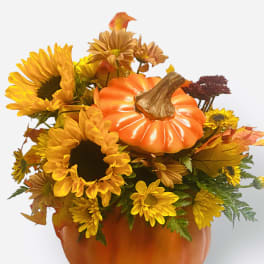 Pumpkin-shaped floral arrangement with sunflowers and autumn mums in an orange container