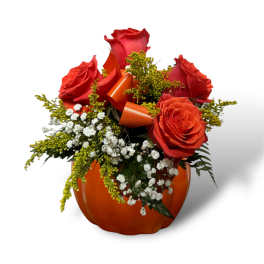 Red roses arranged in an orange pumpkin-shaped container with ribbon