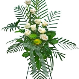 Tall standing spray of white roses with large palm fronds and green accents on an easel.