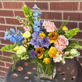 Mixed bouquet in a clear glass vase with blue, pink, yellow, and purple flowers