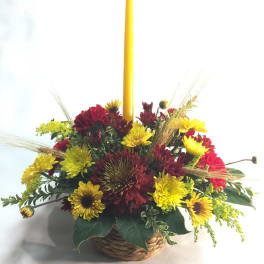 Basket arrangement of yellow and red flowers with a tall yellow candle