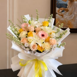 Bouquet of pink, yellow, and white flowers wrapped in white paper with a yellow ribbon