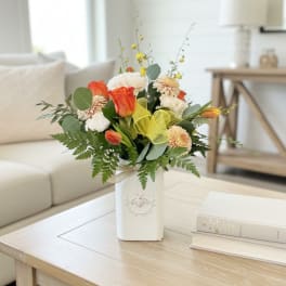 Orange and white flower arrangement in a white vase on a coffee table