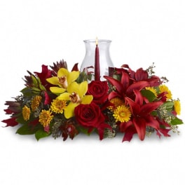 Red and yellow floral centerpiece with a candle in a glass vase