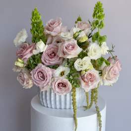 Pink and white roses arranged in a white vase with green spikes