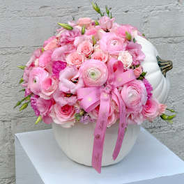 Pink floral arrangement in a white pumpkin-shaped vase with a ribbon bow