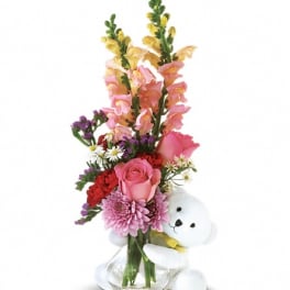 Pink and red flower arrangement with a white teddy bear in a glass vase