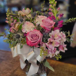 Pink roses and mixed blooms arranged in a glass vase with a white ribbon