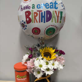 Birthday balloon above a mixed flower arrangement with a candy container
