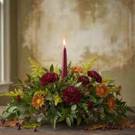 Low floral centerpiece with a lit burgundy candle and orange blooms