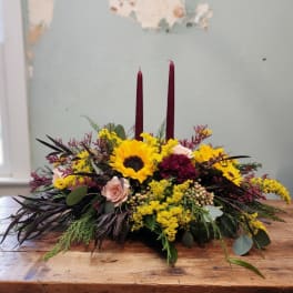 Low floral centerpiece with sunflowers, roses, and burgundy candles