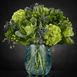 Green floral arrangement in a glass vase with cabbage roses and thistle