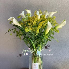White calla lilies and yellow filler flowers in a clear glass vase