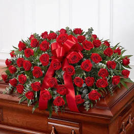 Red rose casket spray with a large red ribbon on a wooden casket
