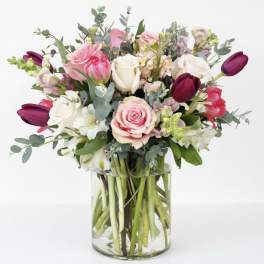 Mixed bouquet of pink, white, and burgundy flowers in a clear glass vase