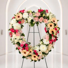 Heart-shaped floral wreath on a metal stand with pink, white, and peach blooms