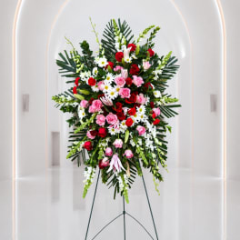 Standing floral spray with red and pink roses, white daisies, and greenery on an easel