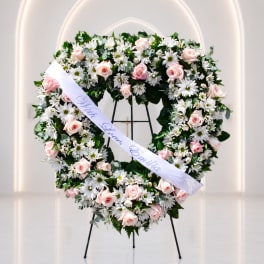 Heart-shaped floral wreath with pink roses and white daisies on a stand