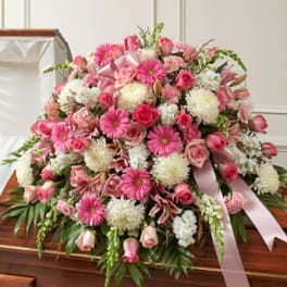 Large pink and white floral casket spray with ribbon on a wooden casket