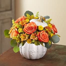 Orange and yellow floral arrangement in a white pumpkin vase