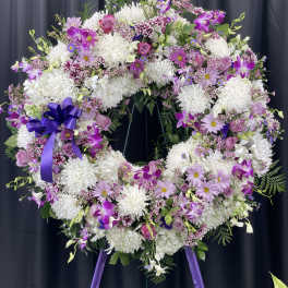Large purple and white floral wreath on a stand with a ribbon bow