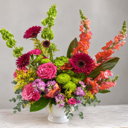 Bright mixed flower arrangement in a white vase with pink, orange, and green blooms