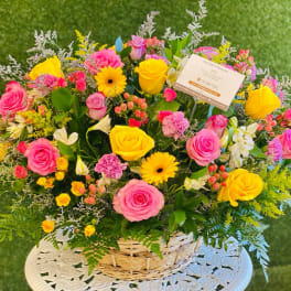 Basket arrangement of pink and yellow roses with mixed flowers