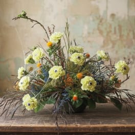 Low floral arrangement with pale yellow blooms in a dark bowl