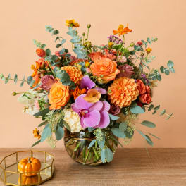 Mixed orange and purple flower arrangement in a glass vase with eucalyptus