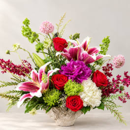 Mixed bouquet with red roses, pink lilies, and purple blooms in a textured vase