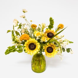 Yellow sunflowers and mixed blooms in a green glass vase