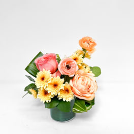 Peach roses and yellow daisies in a green glass vase