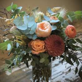 Peach and coral bouquet in a glass vase with blue-green foliage