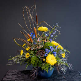 Tall floral arrangement with yellow chrysanthemums and blue flowers in a blue vase
