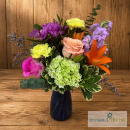 Mixed bouquet in a dark blue vase with roses, lilies, and hydrangea