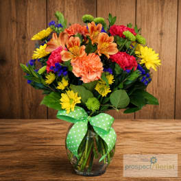 Colorful mixed bouquet in a glass vase with a green polka-dot ribbon