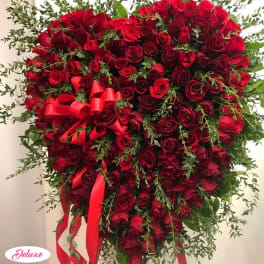 Heart-shaped red rose arrangement with red ribbon and greenery