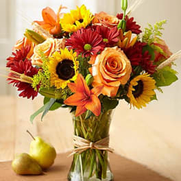 Mixed bouquet of sunflowers, roses, lilies, and red daisies in a glass vase