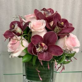Pink roses and burgundy orchids in a square glass vase