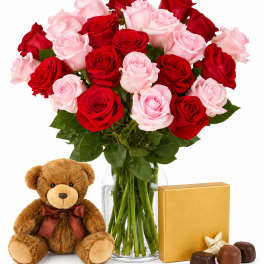 Bouquet of red and pink roses in a glass vase with a teddy bear and chocolates