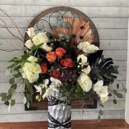 Mixed floral arrangement in a silver vase with white, orange, and dark blooms