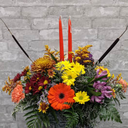 Colorful floral arrangement with two red candles in a dark container